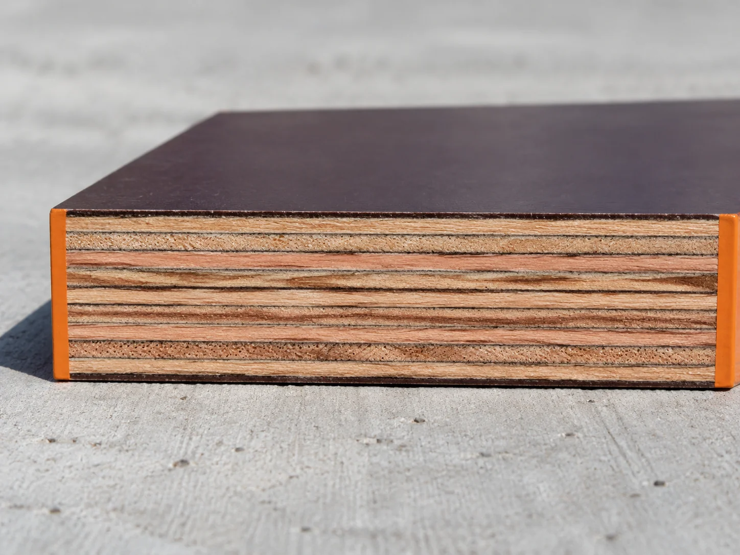 Macro of a cut film-faced plywood edge showing thin dark film on top and bottom and many thin acacia and eucalyptus veneers