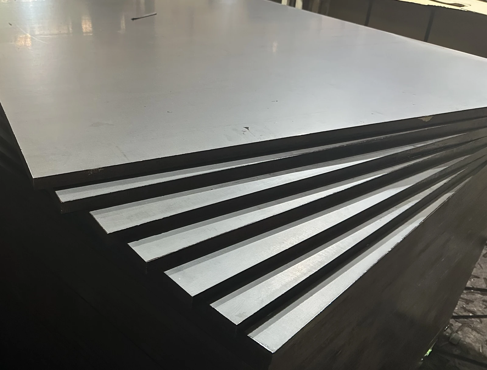 Fanned stack of film-faced plywood sheets showing smooth dark faces and thin edges
